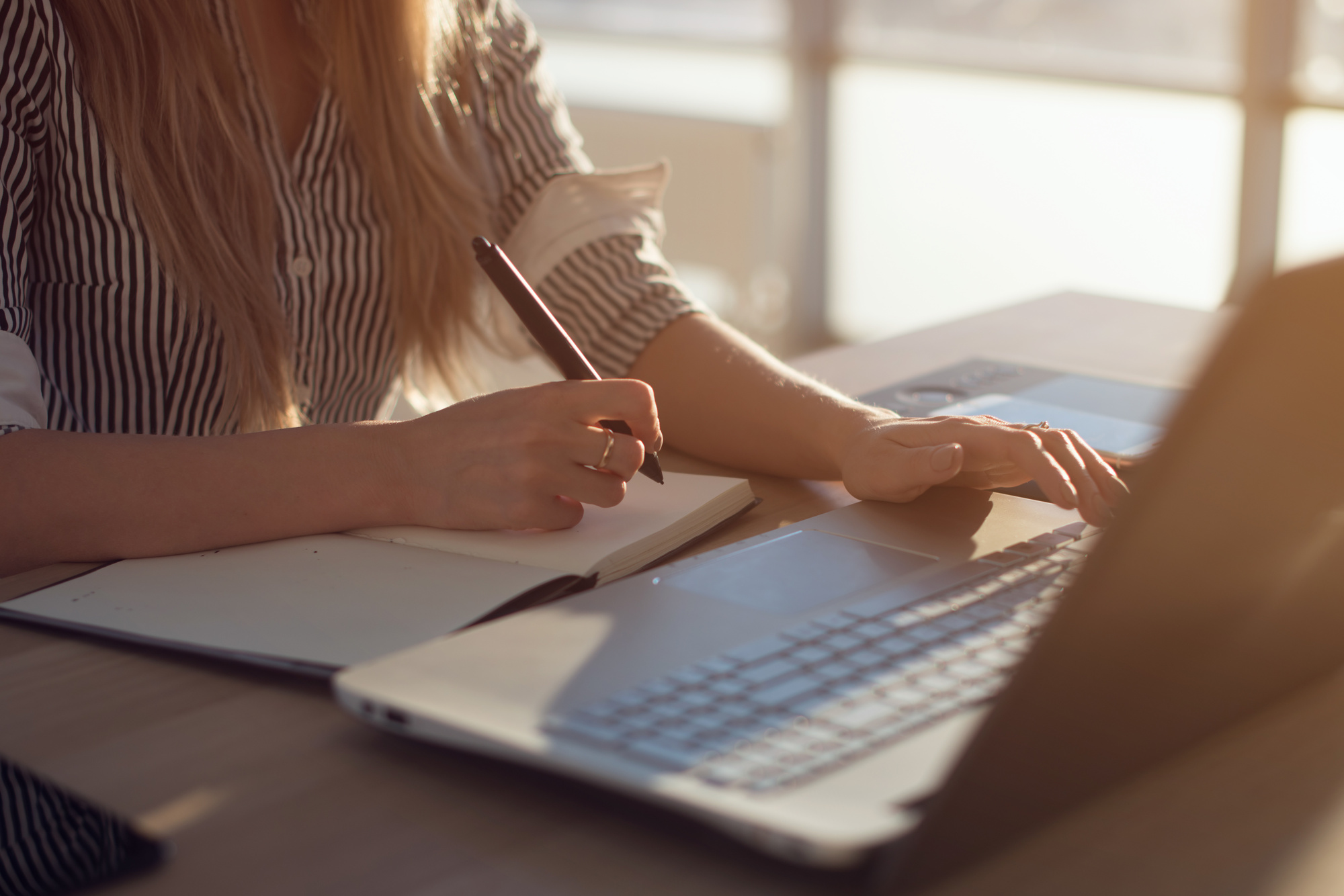 woman writing book and typing on laptop